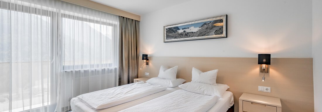 A modern room with two single beds and beautiful daylight. View of a balcony with curtains and a painting on the wall. - Apart Hotel Garni Wieser - Sölden