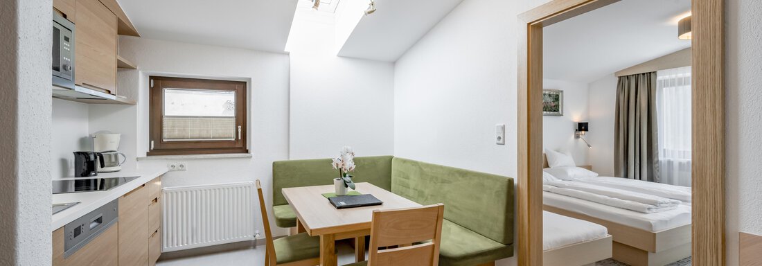 230620_104436 A modern kitchenette with a dining table and chairs. In the background, there is a bedroom with a double bed. - Apart Hotel Garni Wieser - Sölden