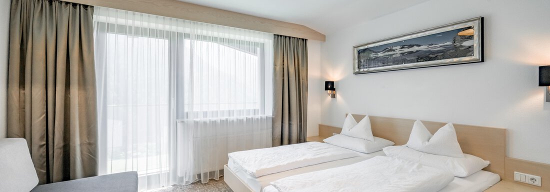 A modern bedroom with two beds and a cozy seating area. Large windows provide plenty of daylight. - Apart Hotel Garni Wieser - Sölden