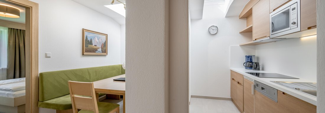 A modern kitchen with wooden cabinets and a small dining area. Bright spaces with natural light and a clock on the wall. - Apart Hotel Garni Wieser - Sölden