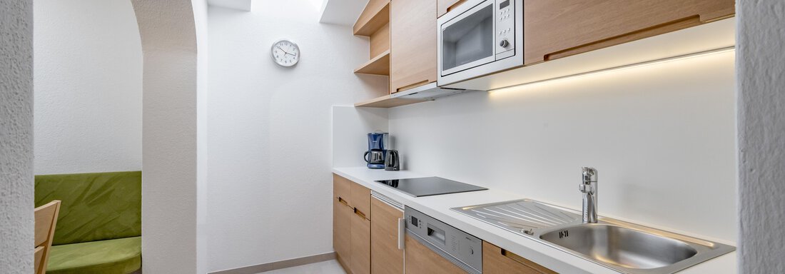 A modern kitchen with wooden cabinets and bright walls. There is a sink, a stove, and a microwave, as well as a small dining area. - Apart Hotel Garni Wieser - Sölden