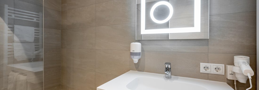 A modern bathroom with a stylish, illuminated wall mirror and a minimalist sink. The walls are neutral in color, creating a relaxed atmosphere. - Apart Hotel Garni Wieser - Sölden