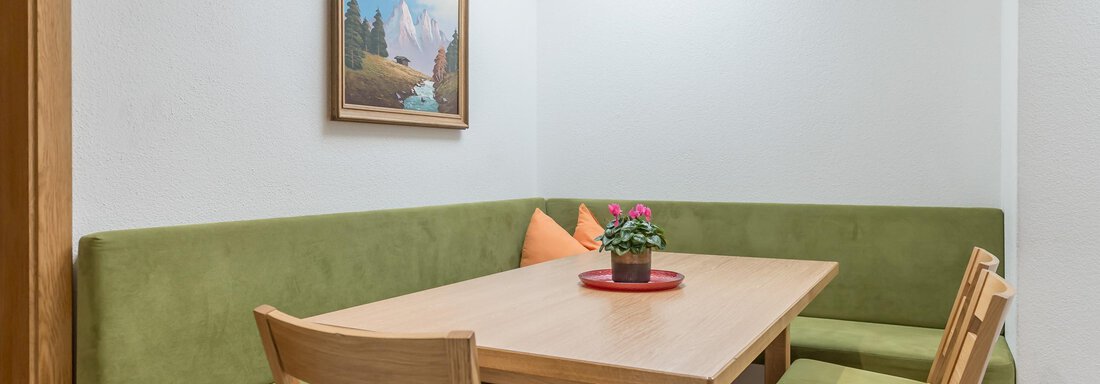 A cozy dining area with a green bench and a wooden table. A picture hangs on the wall, and a plant sits on the table. - Apart Hotel Garni Wieser - Sölden