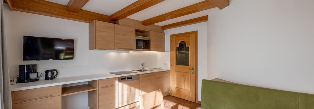 A modern kitchen with a wooden ceiling and full amenities. A dining area with a green sofa and a table is also visible. - Apart Hotel Garni Wieser - Sölden