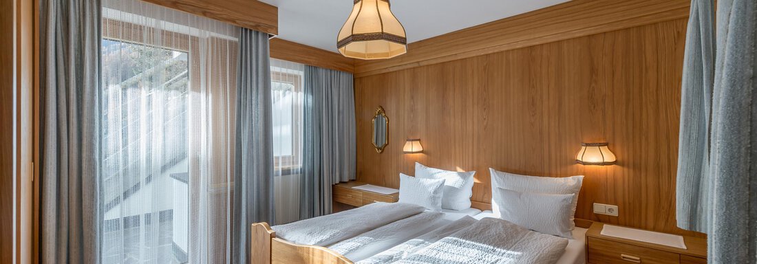A cozy bedroom with wooden paneling and two beds. Large windows provide plenty of daylight and a pleasant atmosphere. - Apart Hotel Garni Wieser - Sölden