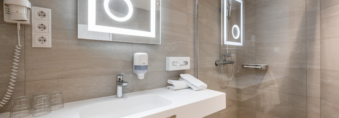 A modern bathroom with a shower and a large mirror. The walls are in neutral tones, and there are towels and soap dispensers. - Apart Hotel Garni Wieser - Sölden