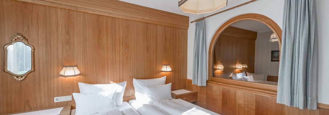 A cozy bedroom with wooden paneling and two beds. The room features a mirror and soft lighting. - Apart Hotel Garni Wieser - Sölden