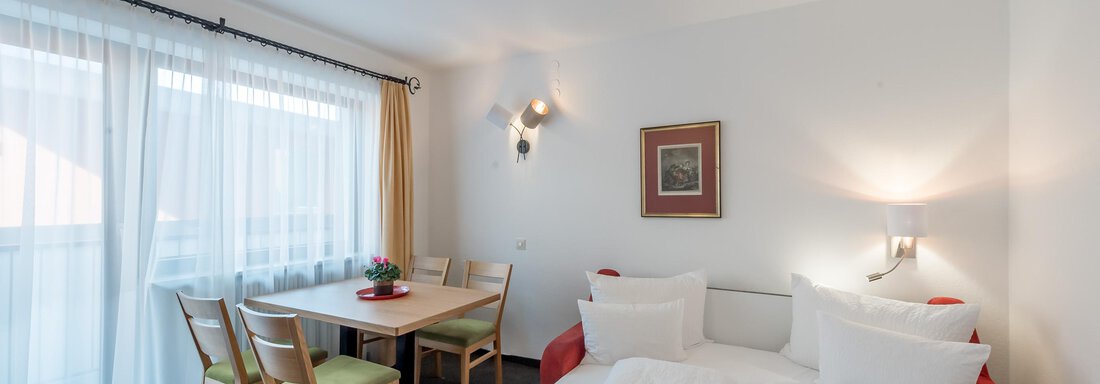 A cozy room with two beds, a dining table, and chairs. Large windows provide plenty of daylight. - Apart Hotel Garni Wieser - Sölden