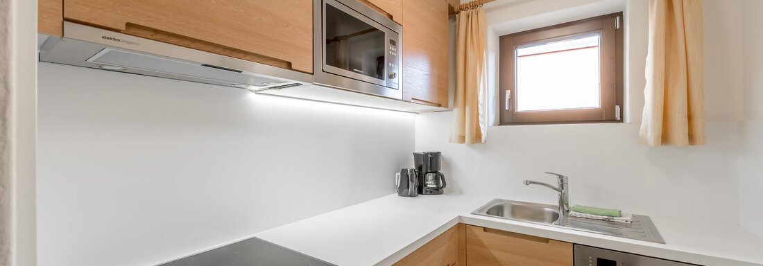 A modern kitchen with wooden cabinets and white surfaces. It includes a refrigerator, a sink, and state-of-the-art kitchen appliances. - Apart Hotel Garni Wieser - Sölden