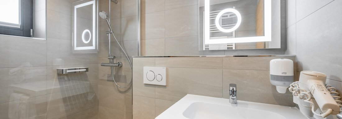 A modern bathroom with a shower and a lighted mirror. The walls are in neutral tones and there are practical features. - Apart Hotel Garni Wieser - Sölden