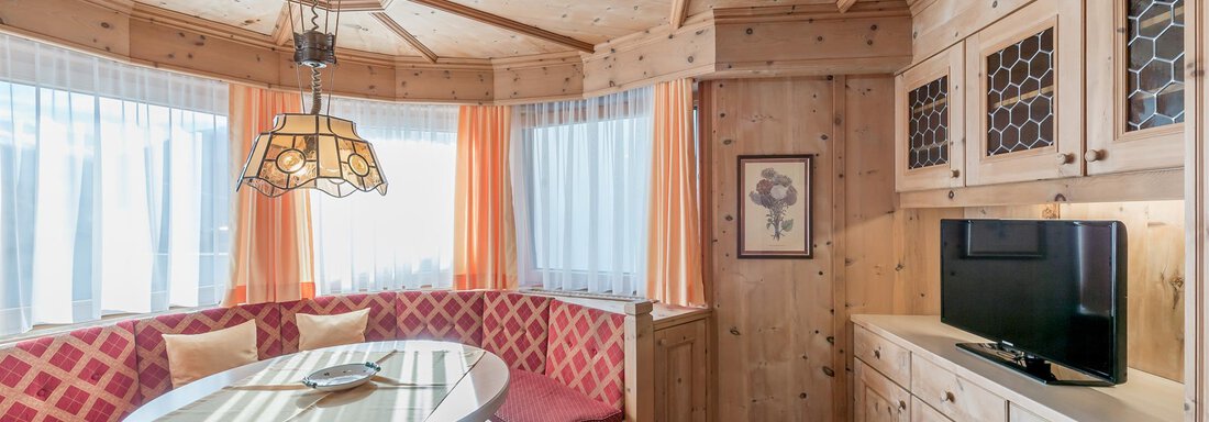 App 11 - Wohnbereich mit Erker A cozy living space with wooden paneling and a round seating area. A table and a television complete the ambiance. - Apart Hotel Garni Wieser - Sölden