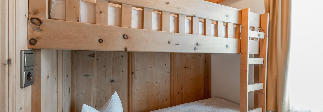 A cozy room with a wooden bunk bed. There are two beds with white pillows and a window with curtains visible. - Apart Hotel Garni Wieser - Sölden