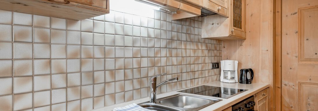 A modern kitchen with wood-paneled cabinets and light tiles. The amenities include a sink, a stove, and a coffee machine. - Apart Hotel Garni Wieser - Sölden
