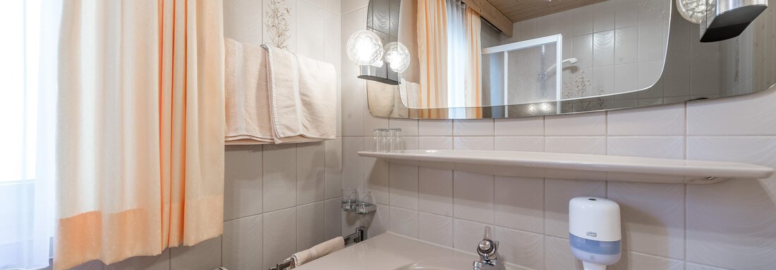 A bright bathroom with a modern sink and a large mirror. The walls are light-tiled and there are curtains in soft colors. - Apart Hotel Garni Wieser - Sölden