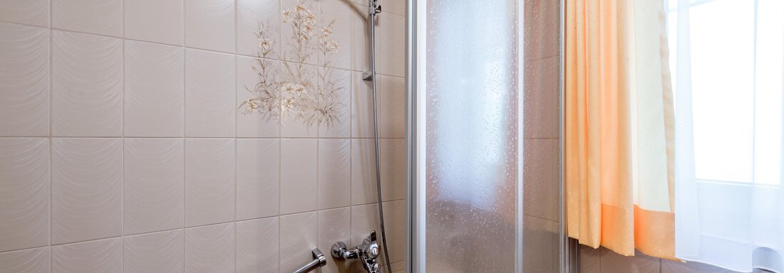 A bathroom with a bathtub and a shower cabin. The window is equipped with a light curtain. - Apart Hotel Garni Wieser - Sölden