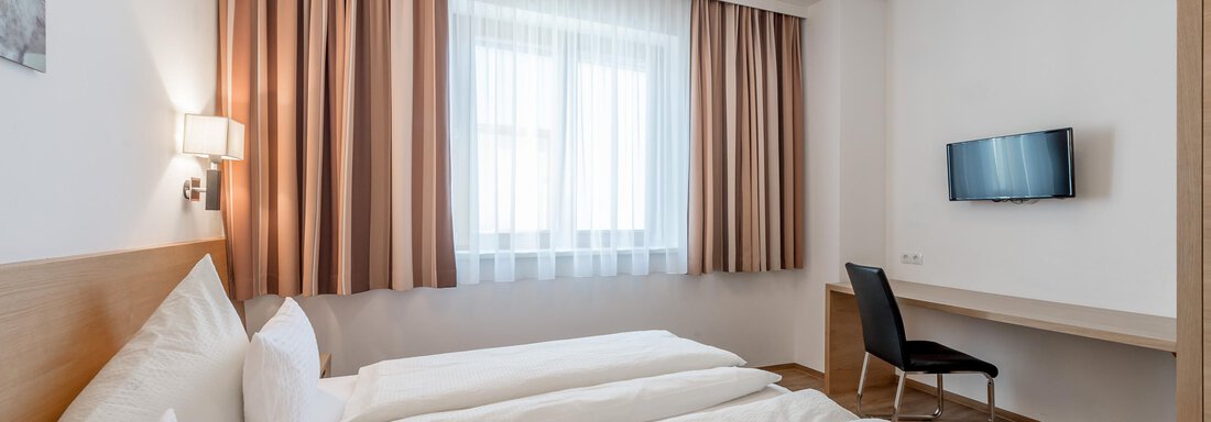 A modern hotel room with two single beds and a desk. It has large windows and light curtains. - Apart Hotel Garni Wieser - Sölden