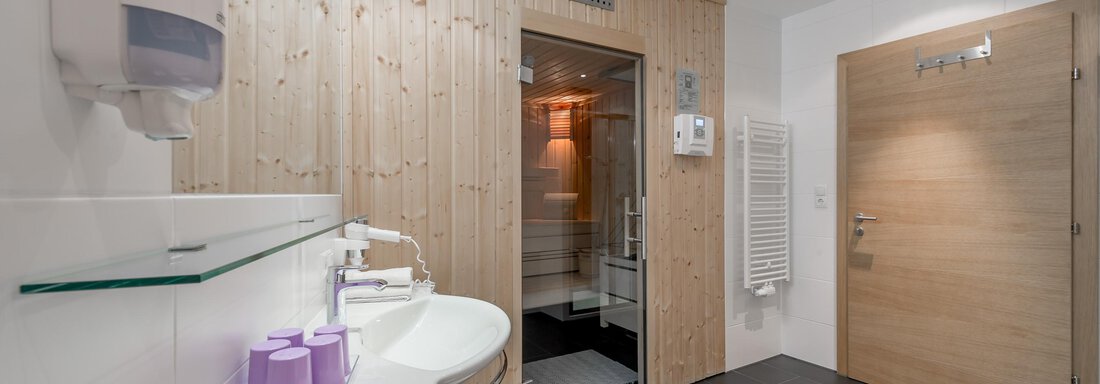A modern bathroom with wooden paneling and elegant lighting. The sink is clean and well-maintained, with a soap dispenser and towel heater. - Apart Hotel Garni Wieser - Sölden