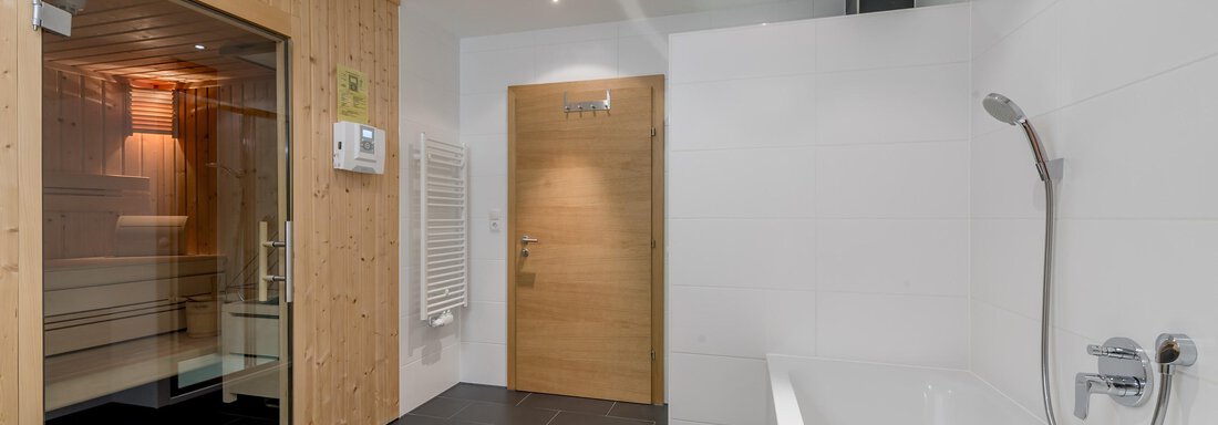 A modern bathroom with a sauna and a freestanding bathtub. The walls are light, and the floor is designed in a dark tile pattern. - Apart Hotel Garni Wieser - Sölden