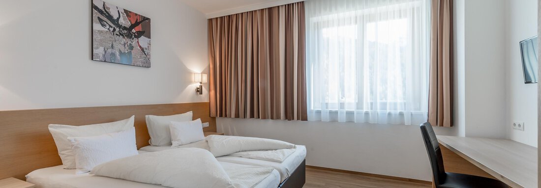 A modern hotel room with two beds, a desk, and large windows. The room is bright and cheerfully furnished. - Apart Hotel Garni Wieser - Sölden