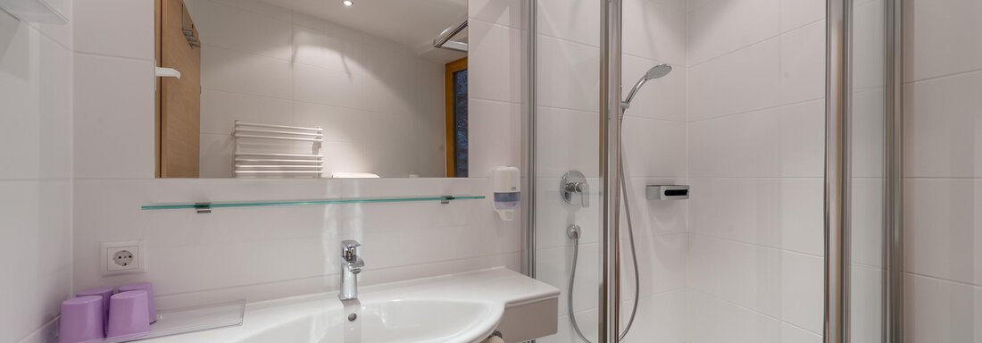 A modern bathroom with a shower and a sink.  
Subtly designed with white walls and a large mirror. - Apart Hotel Garni Wieser - Sölden