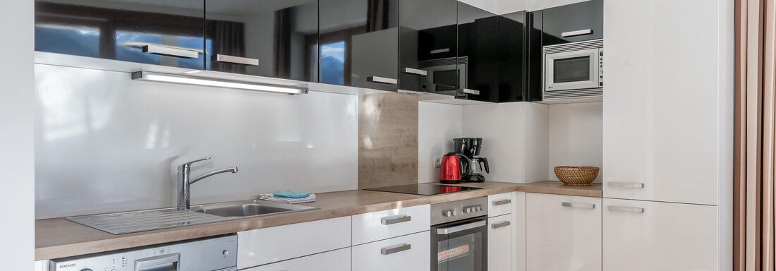 Modern kitchen with white furniture and black upper cabinet. Well equipped with appliances like stove, microwave, and refrigerator. - Apart Hotel Garni Wieser - Sölden