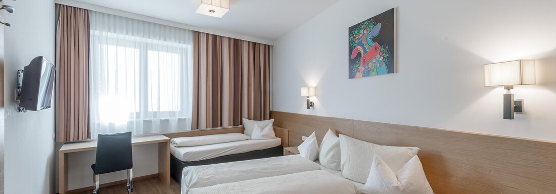 A modern hotel room with two single beds, a desk, and a television. Large windows provide plenty of daylight. - Apart Hotel Garni Wieser - Sölden