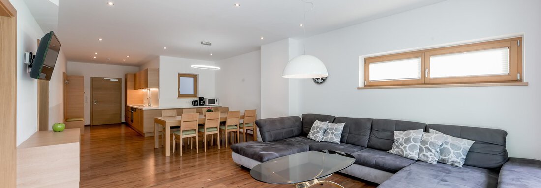 App 13 - Wohn-Essbereich A modern living room with a large, comfortable sofa and a dining table in the background. Bright walls and wooden flooring create a friendly atmosphere. - Apart Hotel Garni Wieser - Sölden
