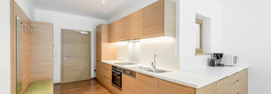 A modern kitchen with wooden cabinets and a bright countertop. The space is friendly and well-lit. - Apart Hotel Garni Wieser - Sölden