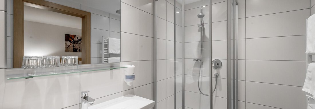 A modern bathroom with a shower and a sink. Bright tiles and a large mirror create an inviting atmosphere. - Apart Hotel Garni Wieser - Sölden