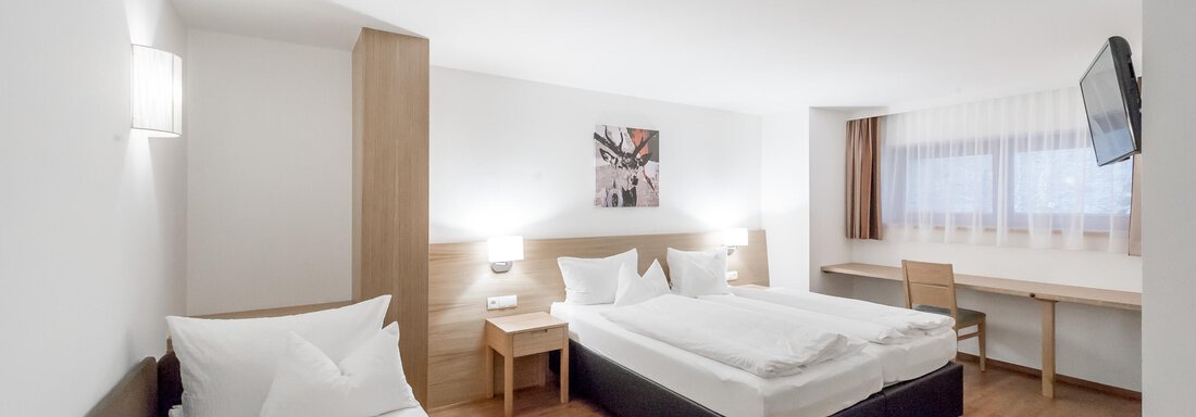 A modern hotel room with two beds and a single bed. There is a desk and soft lighting. - Apart Hotel Garni Wieser - Sölden