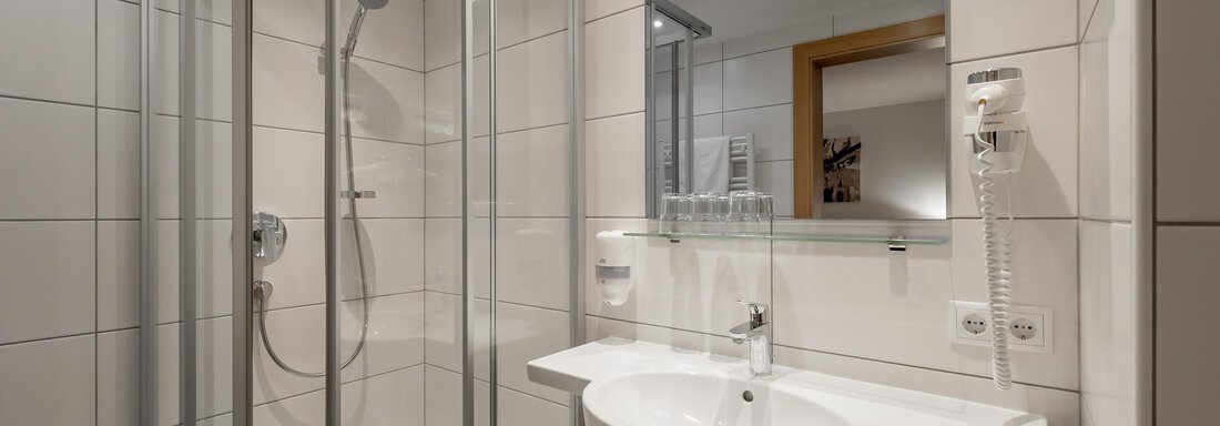 A modern bathroom with a shower and a sink. Bright tiles and a large mirror surface create an inviting atmosphere. - Apart Hotel Garni Wieser - Sölden