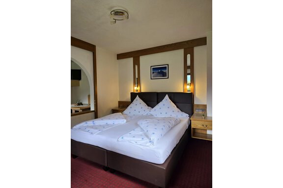 A cozy bedroom with a large bed and white pillows. The walls are painted in warm tones, and a picture hangs above the bed. - Apart Tyrolis - Sölden