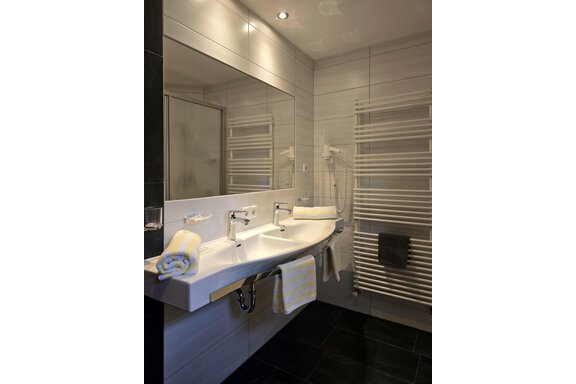 A modern bathroom with two sinks and large mirrors. Bright tiles and towels create an inviting atmosphere. - Apart Tyrolis - Sölden