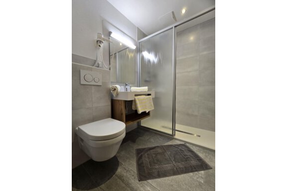 A modern bathroom with a shower, a sink, and a toilet. The wall tiles are in neutral shades of gray. - Apart Tyrolis - Sölden