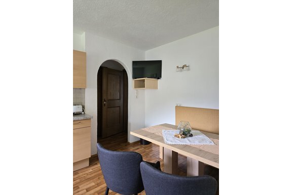 A cozy dining area with a table and two chairs. A television hangs on the wall, and in the background, a modern kitchen is visible. - Apart Tyrolis - Sölden