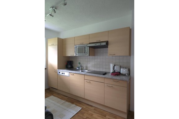 A modern kitchen with light wooden furniture and a granite countertop. It is equipped with a stove, a microwave, and other kitchen appliances. - Apart Tyrolis - Sölden