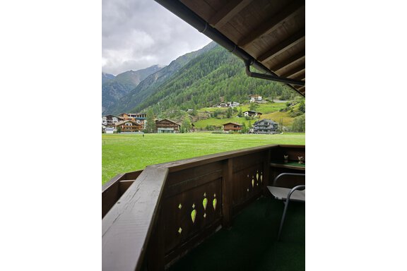 A cozy terrace overlooking a green meadow and surrounding mountains. In the background, several traditional chalets are visible. - Apart Tyrolis - Sölden