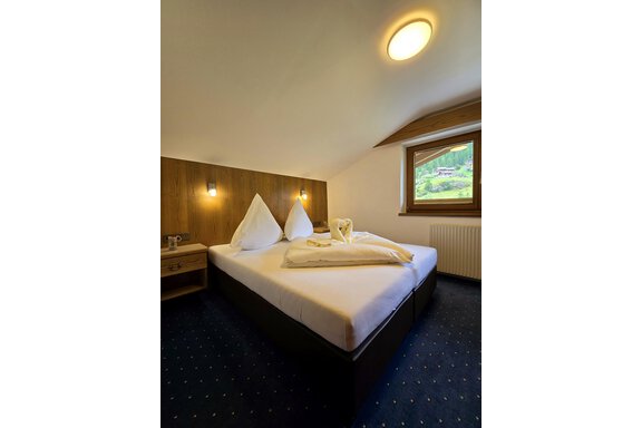 20240702_181734 A cozy bedroom with a large bed and wood-paneled walls. Freshly folded towels are lying on the bed, and there is a view outside through the window. - Apart Tyrolis - Sölden