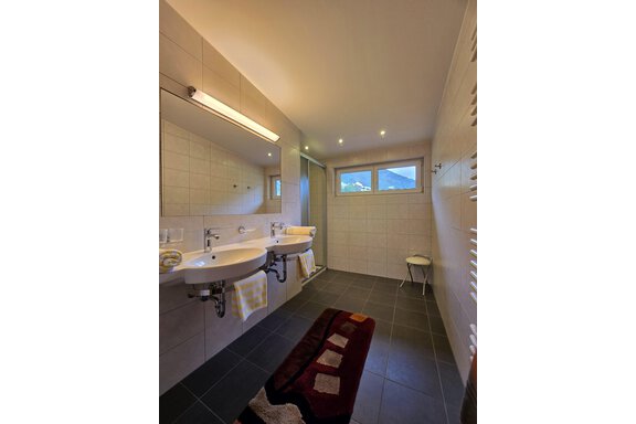 A modern bathroom with two sinks and a shower. Large windows let in plenty of light. - Apart Tyrolis - Sölden