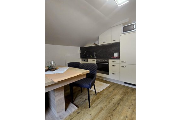 A cozy kitchen with modern appliances and a dining table. The walls are light-colored, and the floor is made of wood. - Apart Tyrolis - Sölden
