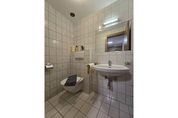 A modern bathroom with white tiles, a sink, and a toilet. The light is bright and there are towels in yellow. - Apart Tyrolis - Sölden