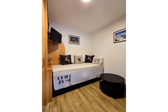A cozy room with a daybed, several pillows, and a small table. Pictures hang on the wall and a television is mounted. - Apart Tyrolis - Sölden