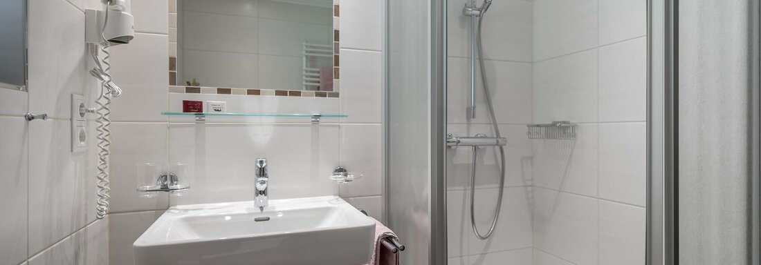 A modern bathroom with a shower and a sink. The walls are designed with light tiles, and a mirror hangs above the sink. - Apart Wiesengrund - Sölden