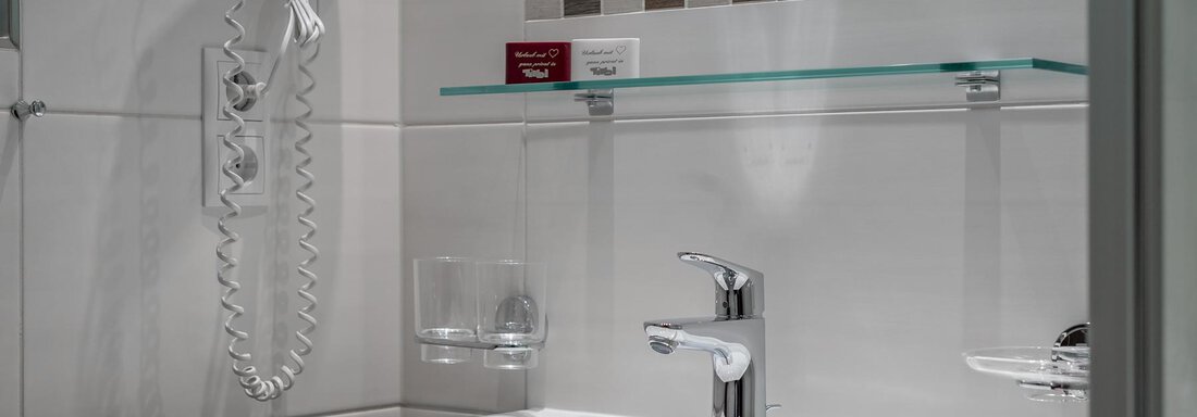 A modern bathroom with a white sink and an elegant faucet. Towel racks and a mirror are mounted on the wall. - Apart Wiesengrund - Sölden