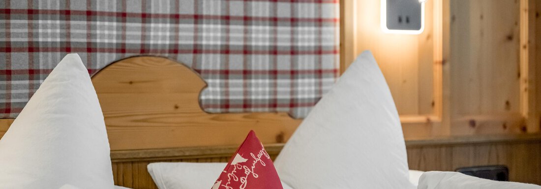 A cozy bedroom with a wooden ceiling and checkered curtains. White pillows and a red pillow give the room an inviting atmosphere. - Apart Wiesengrund - Sölden
