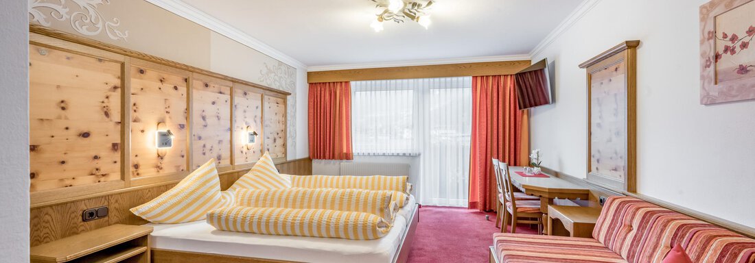 A cozy hotel room with two beds and wooden paneling. There is a small table and a seating area with a red carpet. - Apart Wiesengrund - Sölden