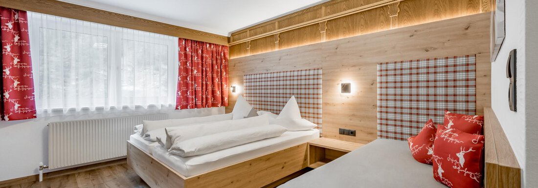 A cozy hotel room with wood decor and modern furniture. There are two beds, a large window area with flared curtains, and warm colors. - Apart Wiesengrund - Sölden