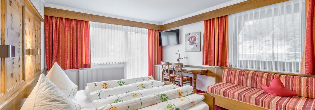 A cozy hotel room with two beds and fresh towels. There is a small table and a couch as well as bright windows with curtains. - Apart Wiesengrund - Sölden