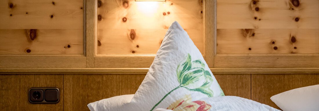 A cozy room with wooden paneling and a warm light source. Decorative pillows with floral patterns are lying on the bed. - Apart Wiesengrund - Sölden