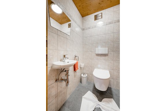 A modern bathroom with tiled walls and a wooden ceiling. There is a sink, a toilet, and a towel rack. - Apart Wiesengrund - Sölden